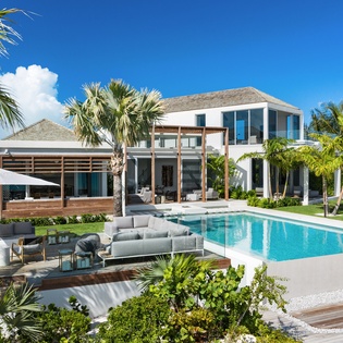Modern luxury villa featuring pristine swimming pool and tropical landscaping under brilliant blue skies.