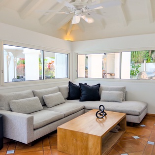 Sink into the plush sectional where natural light fills every corner, inviting you to unwind beneath the gentle hum of the ceiling fan as your tropical getaway unfolds.