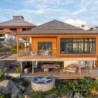 A stunning contemporary villa with warm wood exteriors and multiple levels set among tropical landscaping and natural stone formations.