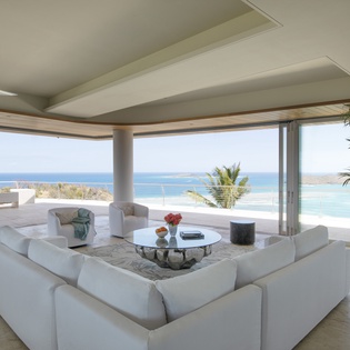 Stunning oceanfront living room with panoramic sea views through floor-to-ceiling windows, perfect for your tropical escape.