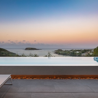 Infinity pool edge frames breathtaking ocean vistas and dramatic sunset skies across the coastal landscape.