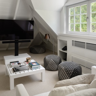 Your cozy attic retreat features modern comfort with plush seating, entertainment center, and peaceful garden views through charming windows.