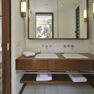Your ensuite bathroom features double sinks with sleek walnut vanity and serene views of natural stonework outside.