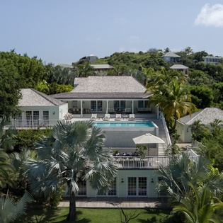 Tropical villa estate with swimming pool nestled among lush Caribbean hillside vegetation and neighboring properties.