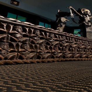 A museum or cultural center display featuring intricate carved artifacts and traditional sculptures in an elegant exhibition space.