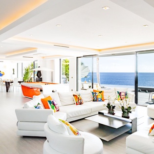 Sink into plush white sofas while soaking up endless ocean views through floor-to-ceiling windows in this bright, modern living space.