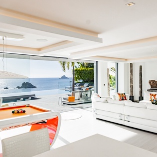 Relax in this stunning oceanfront living space where floor-to-ceiling windows frame breathtaking sea views, while you unwind on plush white sofas.