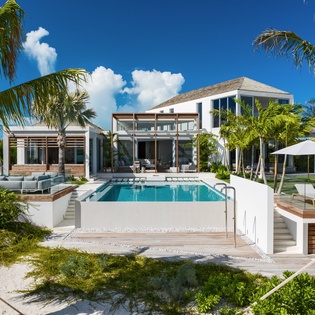 A stunning tropical villa with crystal-clear pool surrounded by swaying palms under brilliant blue skies.