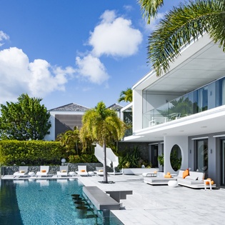 Modern luxury villa with infinity pool overlooking pristine waters, surrounded by tropical palm trees and contemporary architecture.