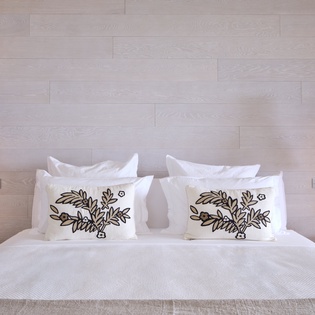 Sink into crisp white linens beneath warm pendant lights, where botanical-print pillows add charm to your peaceful retreat.