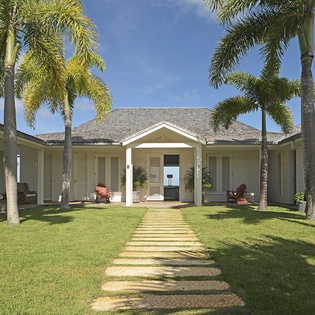 Elegant tropical property featuring a courtyard design with lush palm trees, manicured lawn, and stone pathway leading to the entrance.