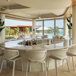 Your curved bar overlooks tropical pools where cocktails taste better with ocean breezes flowing through floor-to-ceiling windows.
