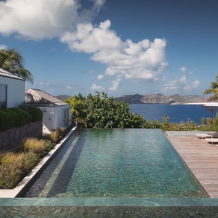 Modern villa featuring infinity pool with panoramic ocean views across tropical waters to distant mountains.