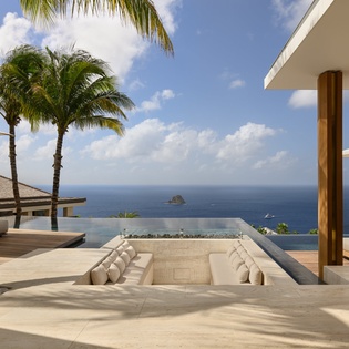 Stunning oceanfront terrace with infinity pool, sunken seating, and panoramic sea views framed by tropical palms.
