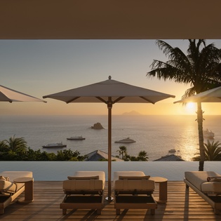 Stunning infinity pool terrace with tropical sunset views over the ocean, featuring luxury loungers and palm trees.