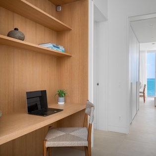 Your dedicated workspace features warm wood built-ins with a view of the sparkling ocean beyond.