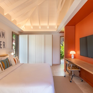 Rest easy in your modern bedroom featuring exposed beams, vibrant orange accent wall, and workspace for productivity.