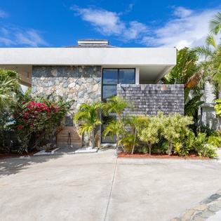 Modern tropical villa featuring contemporary stone architecture surrounded by lush palm trees and vibrant landscaping.