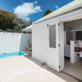 Step from your cozy bedroom directly onto a sunny terrace where a private plunge pool awaits—an intimate oasis framed by whitewashed walls, loungers, and blue skies overhead.