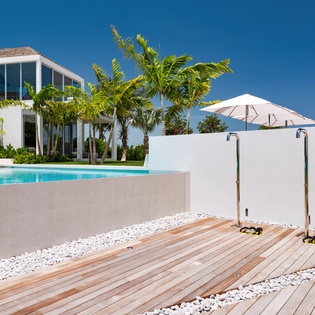 Modern tropical villa with elevated pool, outdoor shower, and palm trees under brilliant blue skies.