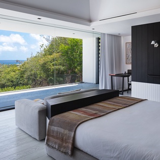Wake up to breathtaking ocean views from your modern bedroom sanctuary, where floor-to-ceiling windows frame tropical paradise beyond.