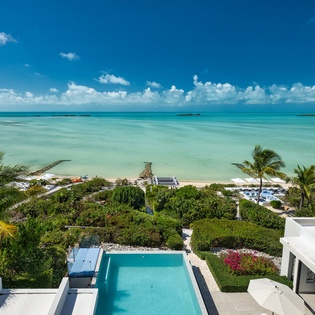 Stunning oceanfront estate with private pool, lush tropical gardens, and pristine turquoise waters stretching to the horizon, surrounded by swaying palms and vibrant island vegetation.