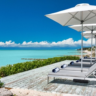 A stunning beachfront scene where turquoise waters and pristine white sand meet lush coastal greenery, framing the property's idyllic tropical setting.