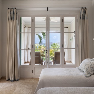 Drift off in a serene bedroom where French doors frame swaying palms and ocean blues, inviting gentle breezes and natural light to lull you into island tranquility.