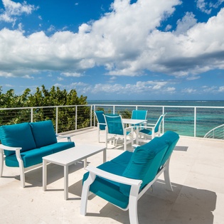 Expansive oceanfront terrace with comfortable seating offers panoramic views of turquoise waters and tropical coastline.