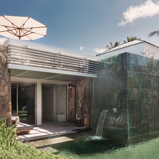 Modern villa exterior featuring contemporary design with natural stone elements and tropical landscaping in a serene setting.