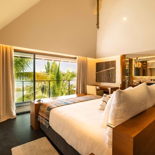 Step into your bright retreat where tropical palms and shimmering water greet you through floor-to-ceiling windows. Sink into plush bedding under vaulted ceilings and let warm natural light fill every corner of your serene escape.