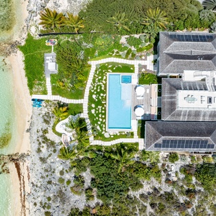 Aerial view of a beachfront villa showcasing the property's layout, swimming pool, lush tropical landscaping, and direct access to pristine turquoise waters and sandy shoreline.