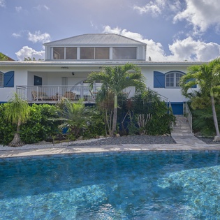 White villa with blue shutters surrounded by lush tropical gardens and private pool area in a beautiful Caribbean setting.