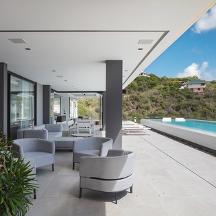 Relax in your sophisticated poolside lounge with modern furniture and stunning views of rolling hills dotted with tropical homes.