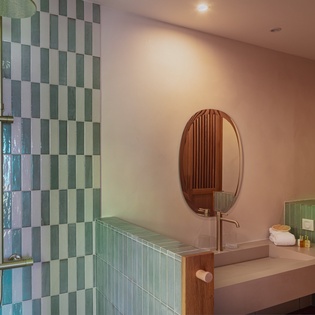 Step into your modern sanctuary featuring glossy seafoam tiles, sleek fixtures, and a warm glow that turns every refresh into a moment of pure relaxation.