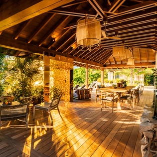 Warm evening light filters through this open-air pavilion, where vaulted wood beams and natural woven lanterns create a welcoming tropical retreat, perfect for dining or unwinding surrounded by lush greenery.
