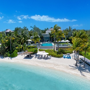 Stunning beachfront villa with pristine white sand beach, turquoise waters, swimming pool, and tropical palm trees creating the perfect island paradise setting.