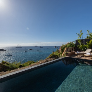 Stunning infinity pool overlooking turquoise waters where sailboats drift peacefully across the horizon.