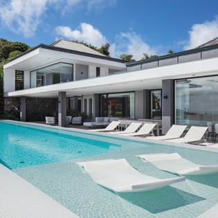 Modern luxury villa featuring expansive pool terrace with crystal-clear waters, contemporary architecture, and lush tropical surroundings.