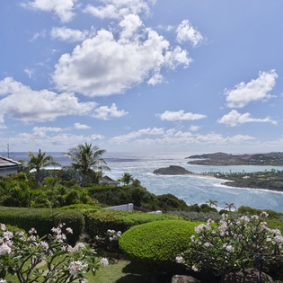 Stunning coastal property surrounded by lush tropical gardens overlooking a picturesque bay and island-dotted horizon under clear blue skies.