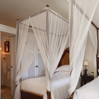Drift into peaceful sleep beneath sheer netting draped around each luxurious bed, with carved wood headboards and crisp white linens inviting you to unwind.