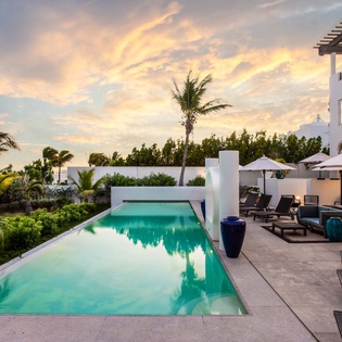 Stunning sunset illuminates the pristine pool and tropical gardens. Sleek white architecture blends with lush palms, creating a tranquil Caribbean-inspired oasis surrounded by modern elegance and natural beauty.