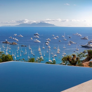 Infinity pool overlooking pristine harbor with luxury yachts and distant mountain vistas.