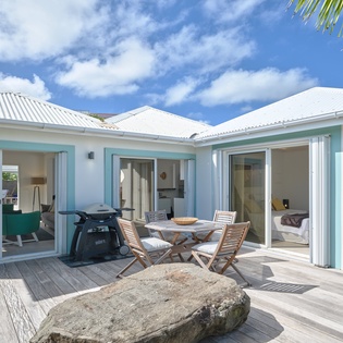 Modern tropical villa with open-plan design featuring turquoise accents and natural stone elements against blue skies.