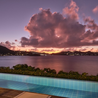 Dramatic sunset paints the sky in vibrant hues over the tranquil bay, with mountains silhouetted against the colorful evening light.