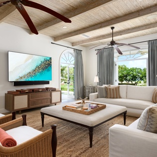 Relax in your spacious living room with vaulted ceilings, cozy seating, and stunning views of lush tropical greenery just beyond the glass doors.