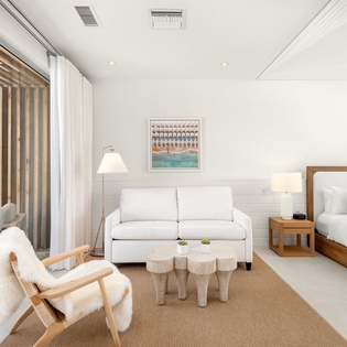 Your elegant retreat features a plush sofa, cozy armchair, and comfortable bed, all bathed in natural light from expansive windows.