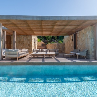 Modern villa featuring a stunning infinity pool and covered outdoor lounge area with natural stone walls.