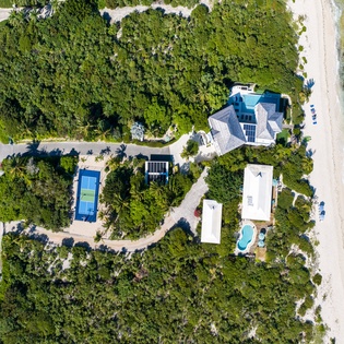 Stunning beachfront estate with tennis court and pool, nestled between tropical vegetation and pristine turquoise waters.