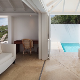 Step through the open doors to your private pool terrace, where bright blue waters and lush greenery await. Relax in the airy sitting area with vaulted ceilings and coastal comfort.